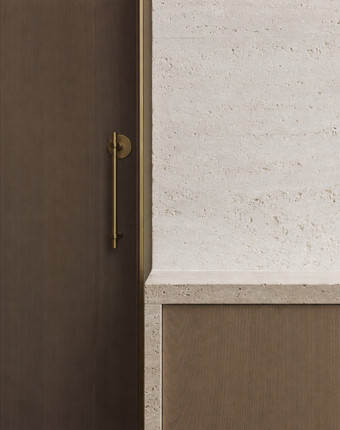 Slender brass pull on a dark walnut door meeting a travertine wall and stone counter edge