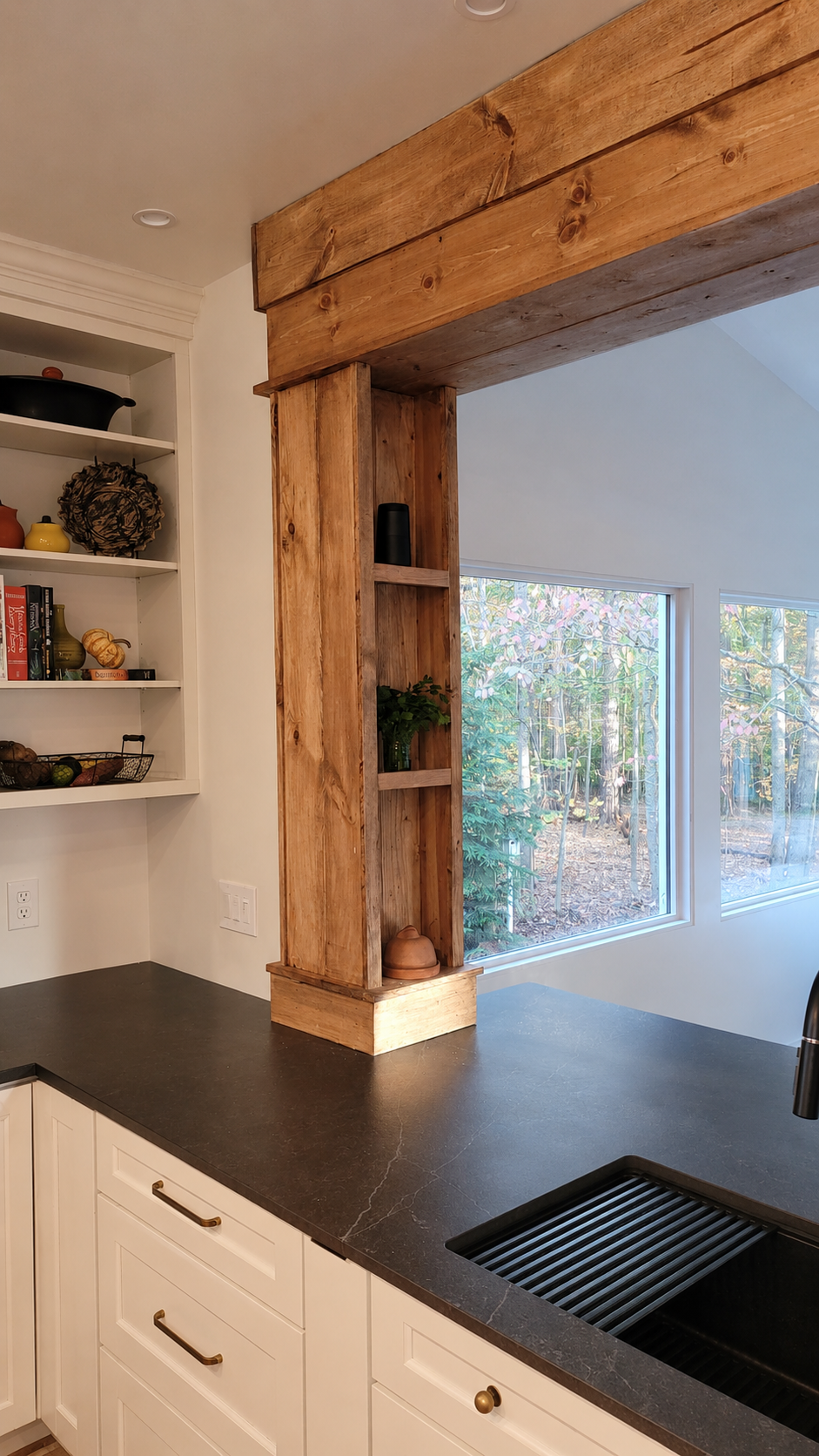 Vertical detail of a reclaimed timber pass-through with brass cabinet pulls and a dark soapstone counter in a Tekee kitchen